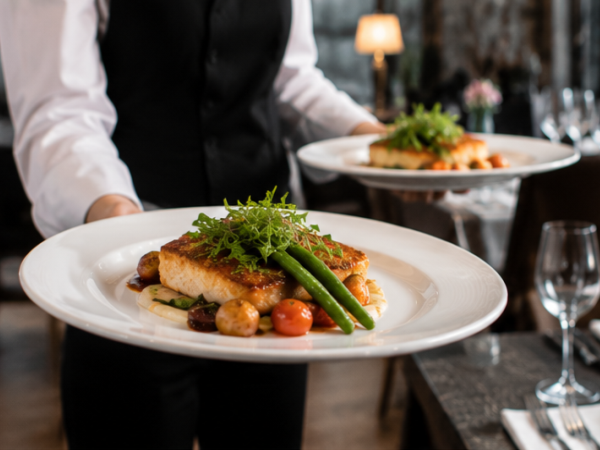 Servicemitarbeiter serviert angerichtete Speisen im Tellerservice an Gäste im Restaurant