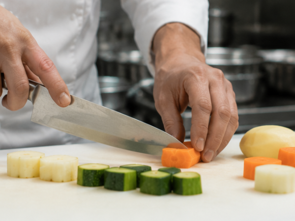 Koch tournierte Gemüse mit einem kleinen Messer in einer professionellen Restaurantküche