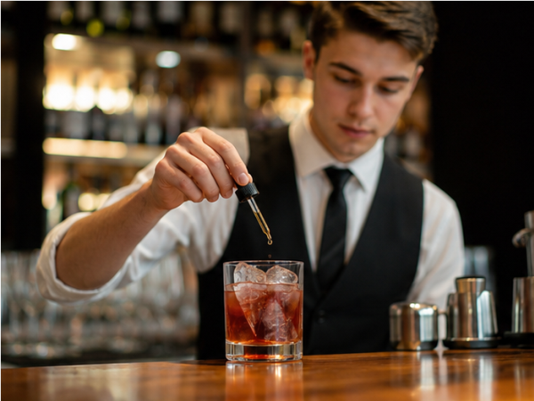 Bartender gibt einen Dash Bitter aus einer Flasche in einen Cocktail im Glas