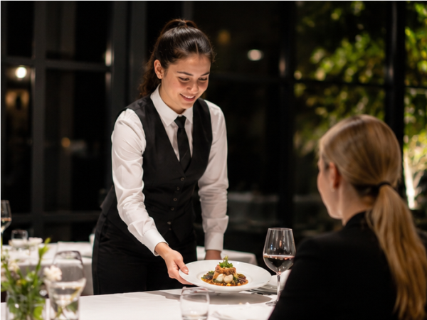Servicemitarbeiter setzt einen Teller mit Speisen fachgerecht vor einem Restaurantgast ein